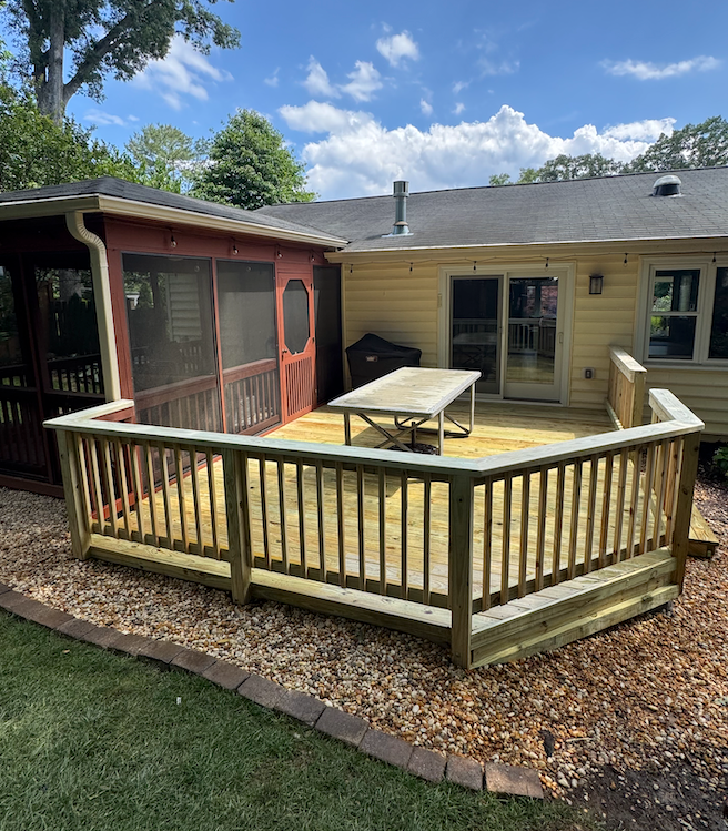 A wooden deck with a table and a screened in porch in front of a house.