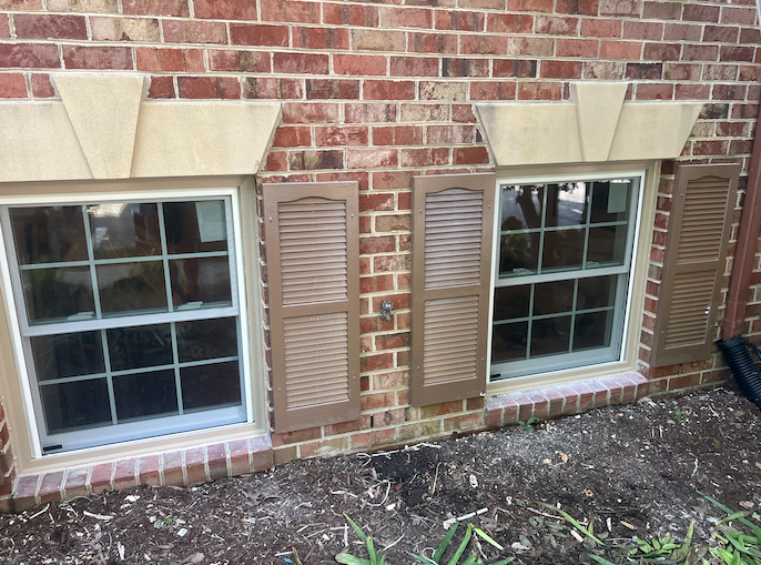 A brick house with two windows and shutters on the side.
