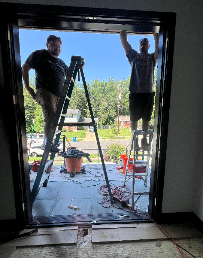 Two men are standing on a ladder in front of a door.