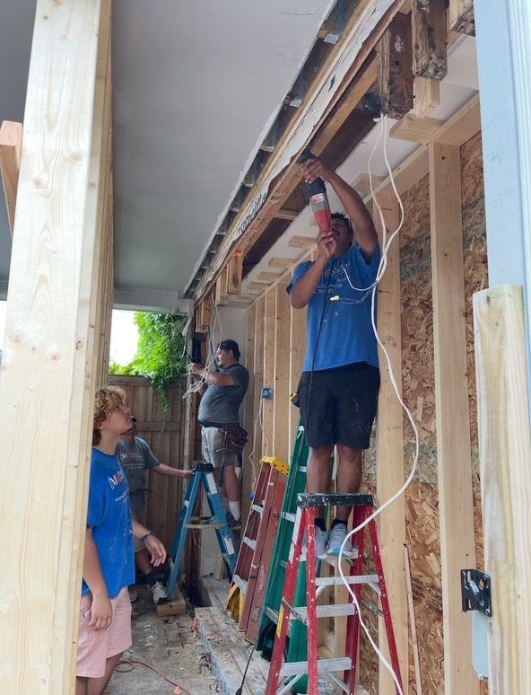 Construction workers wiring a building; working on ladders. Wood framing visible.