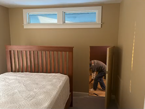 A man is standing in a bedroom next to a bed.