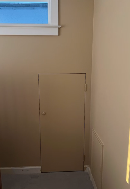 A door in a corner of a room next to a window.
