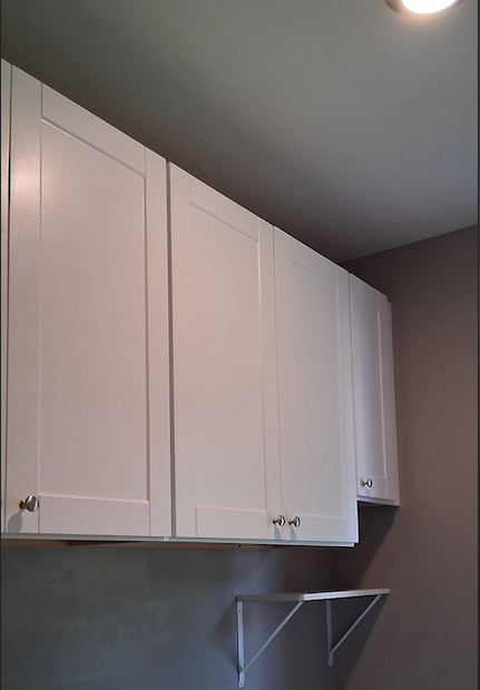 White kitchen cabinets with silver knobs mounted on a gray wall.