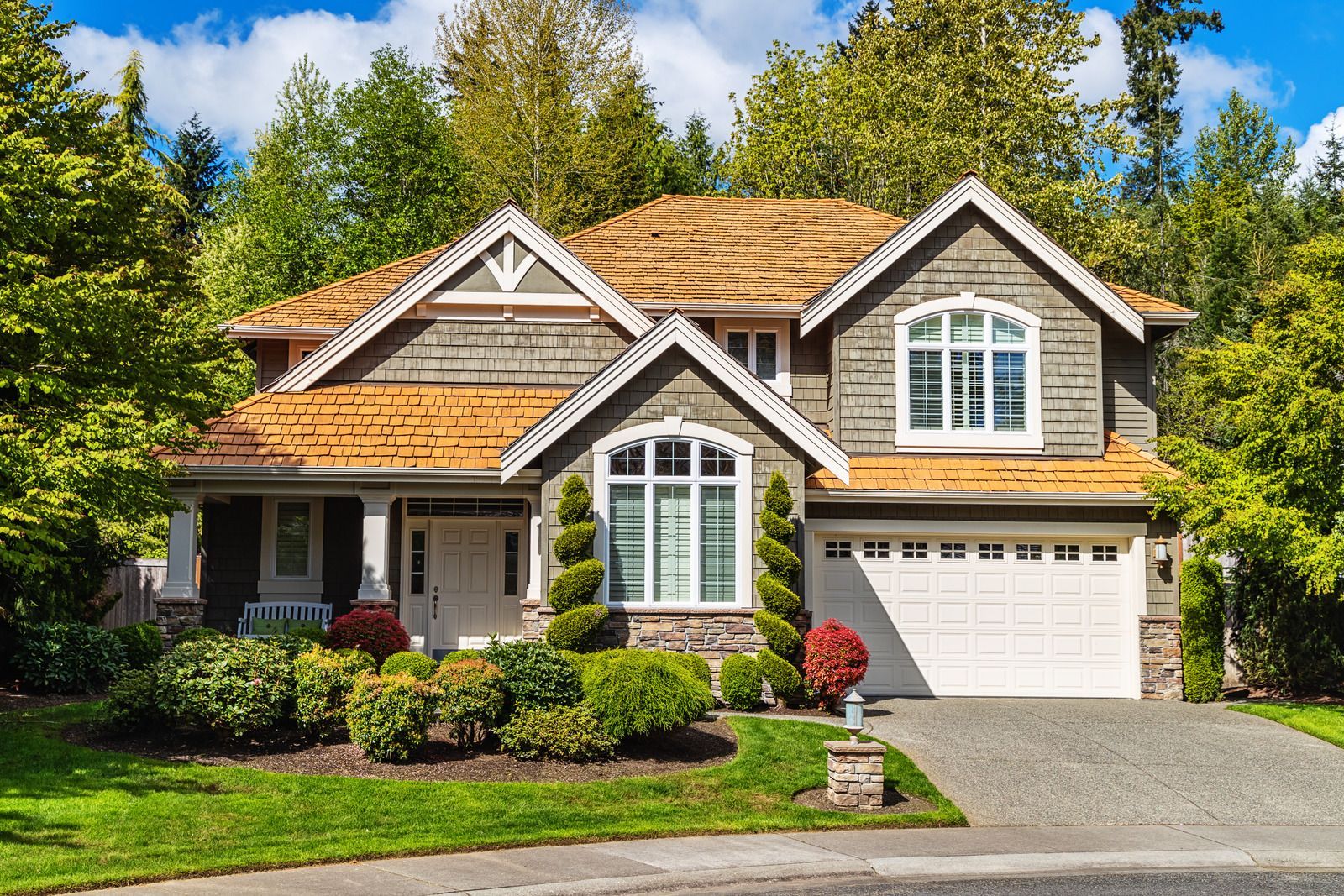 A large house with a wooden roof and a white garage door is surrounded by trees.