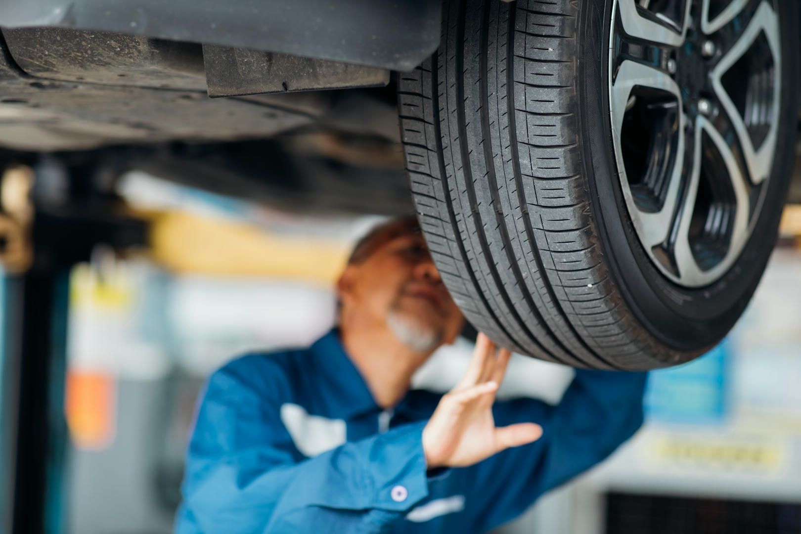 A man is working under a car on a lift in a garage.