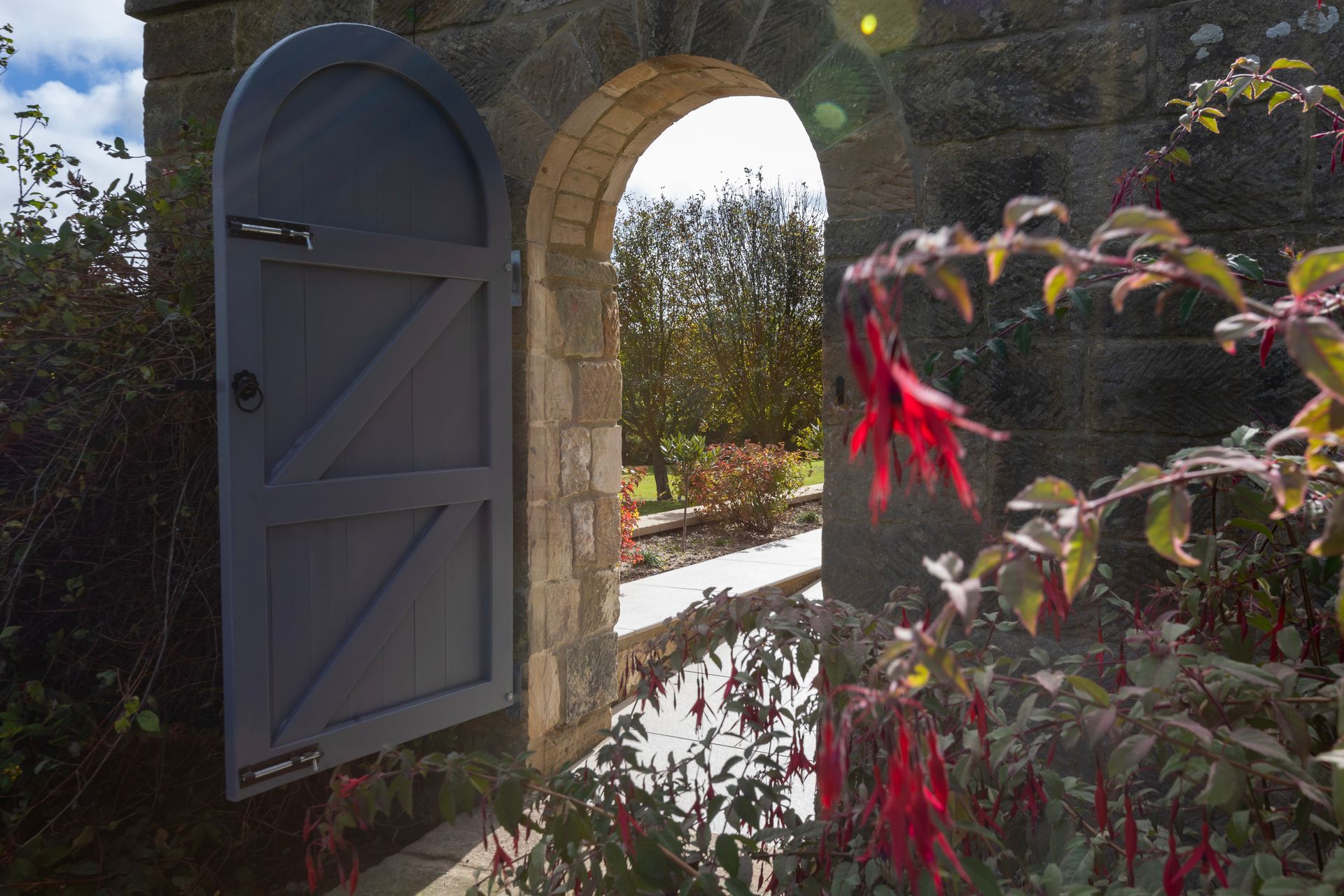 A wooden door is open to a stone archway in a garden.