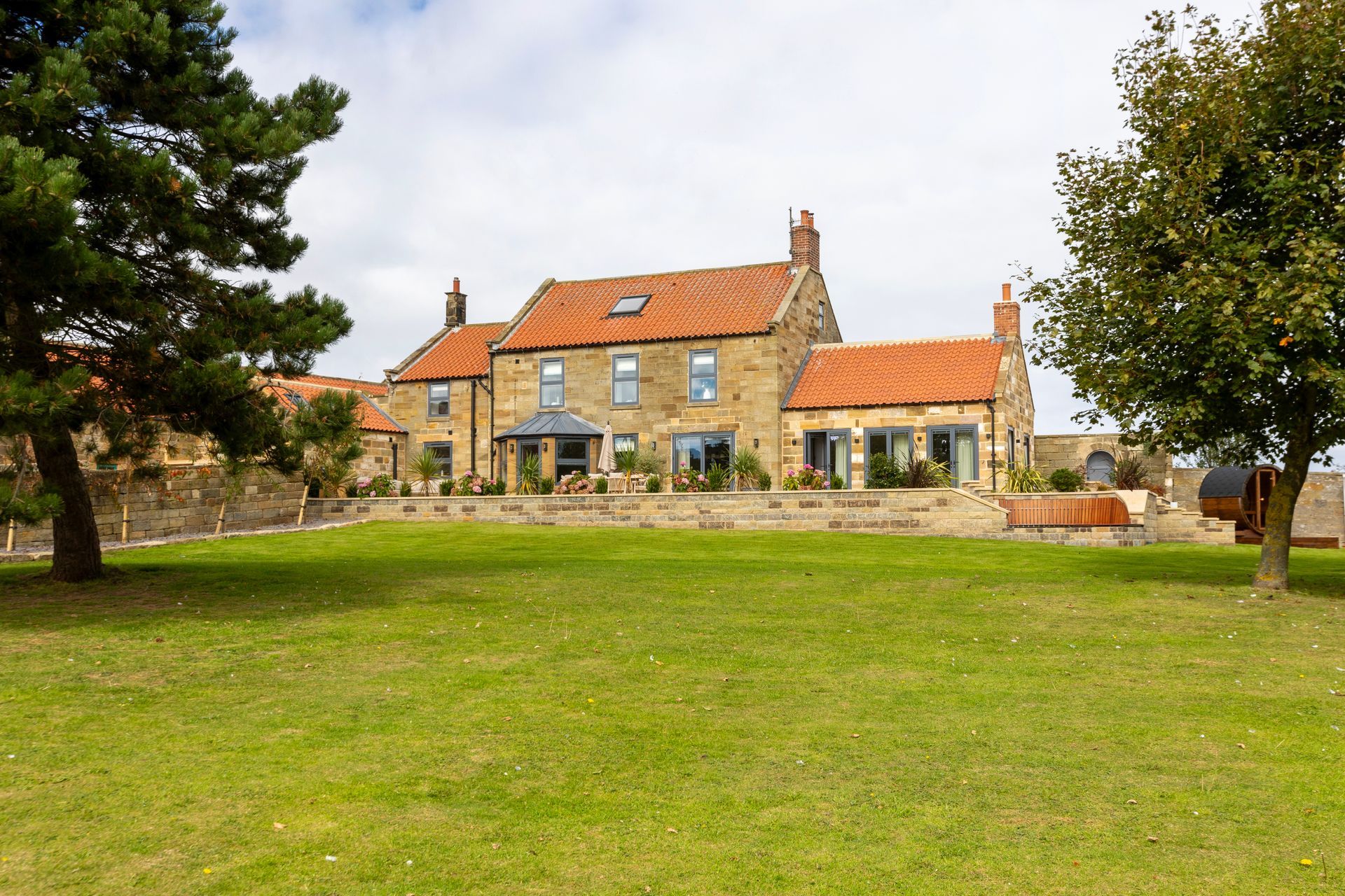 A large house with a red tile roof sits in the middle of a lush green field.