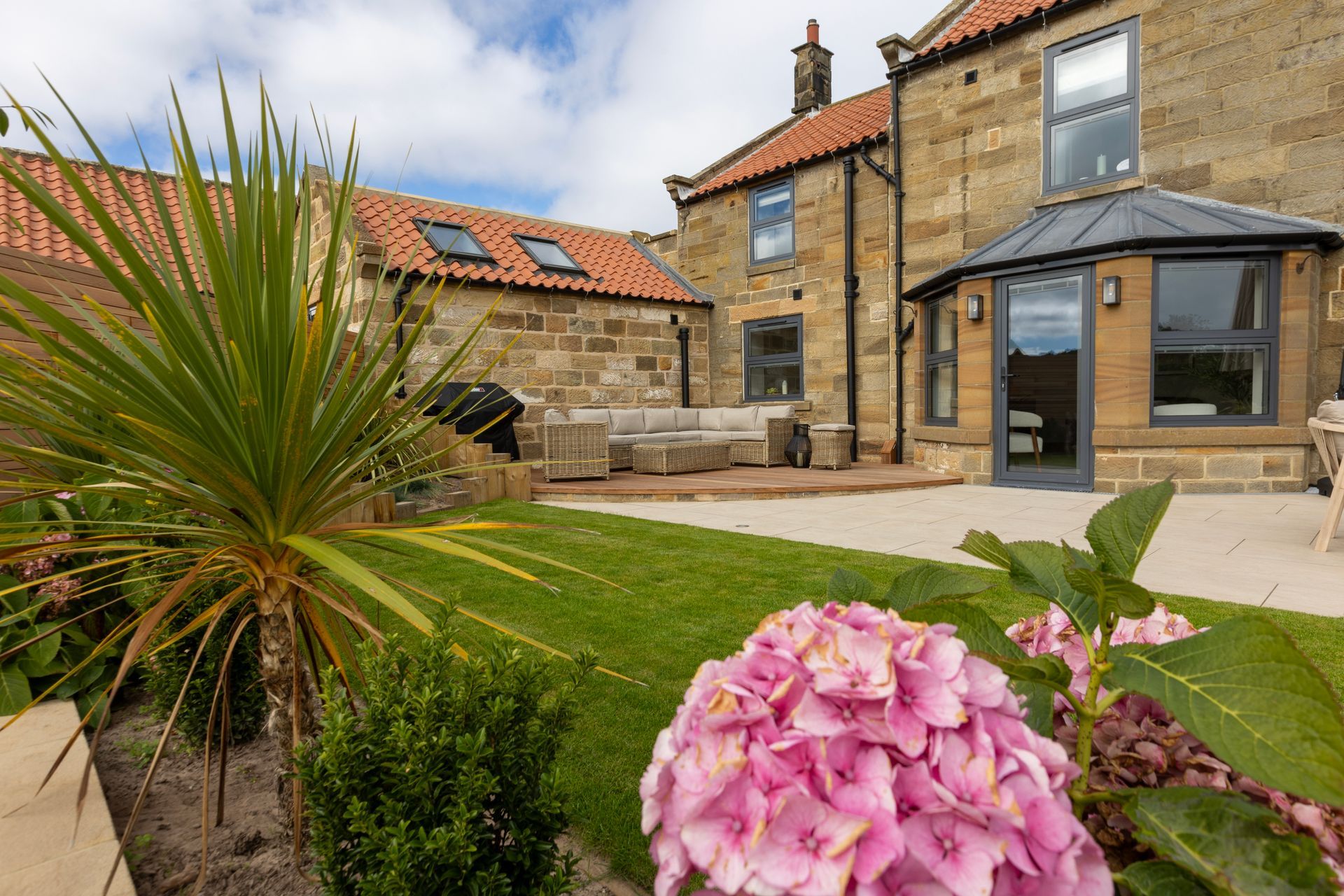 A large stone house with a patio and a pink flower in front of it.