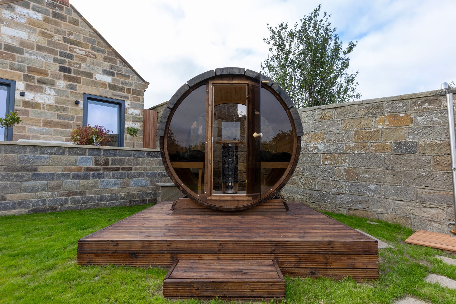 A wooden barrel sauna is sitting on top of a wooden deck in a backyard.