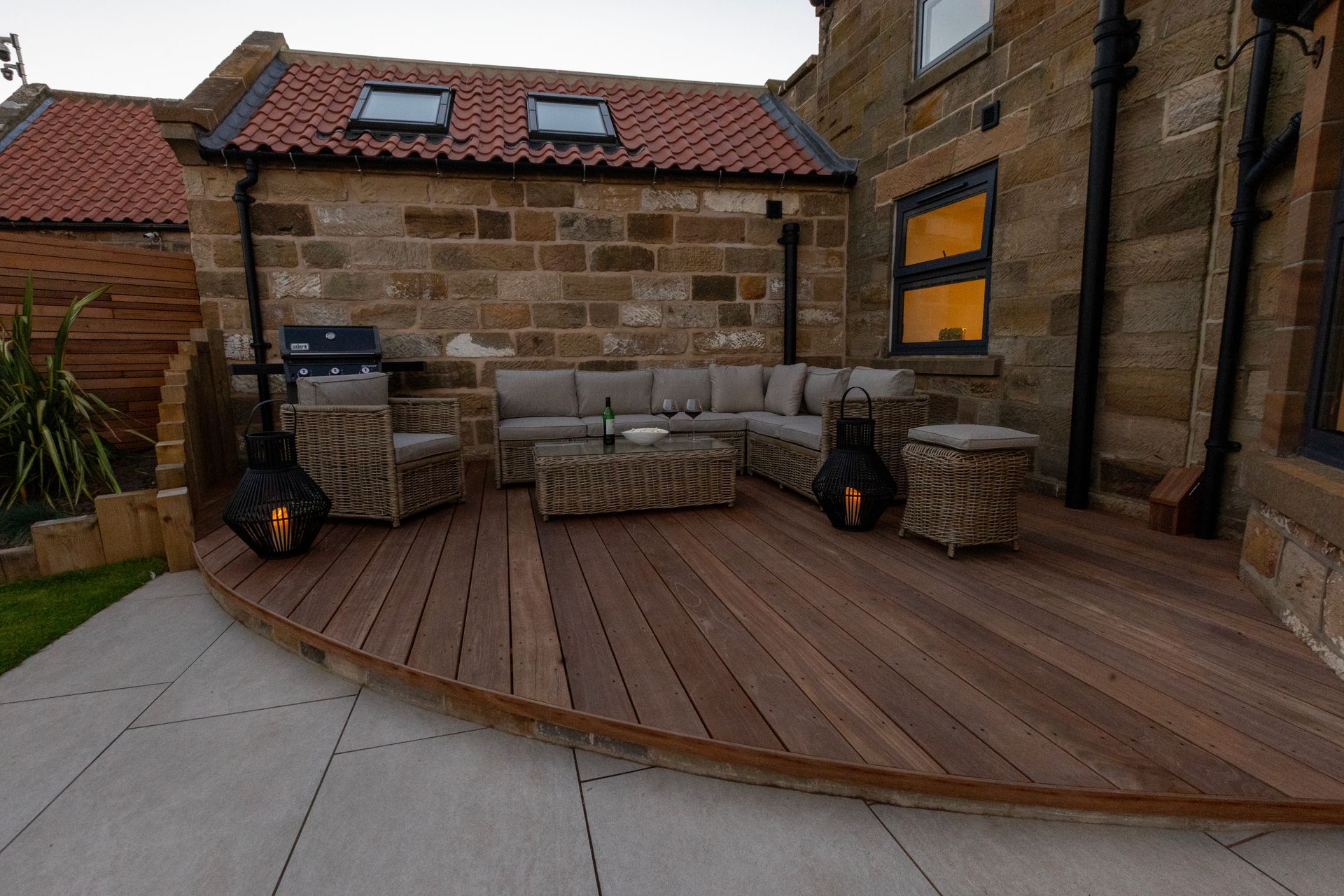 A wooden deck with a couch and chairs on it in front of a brick building.