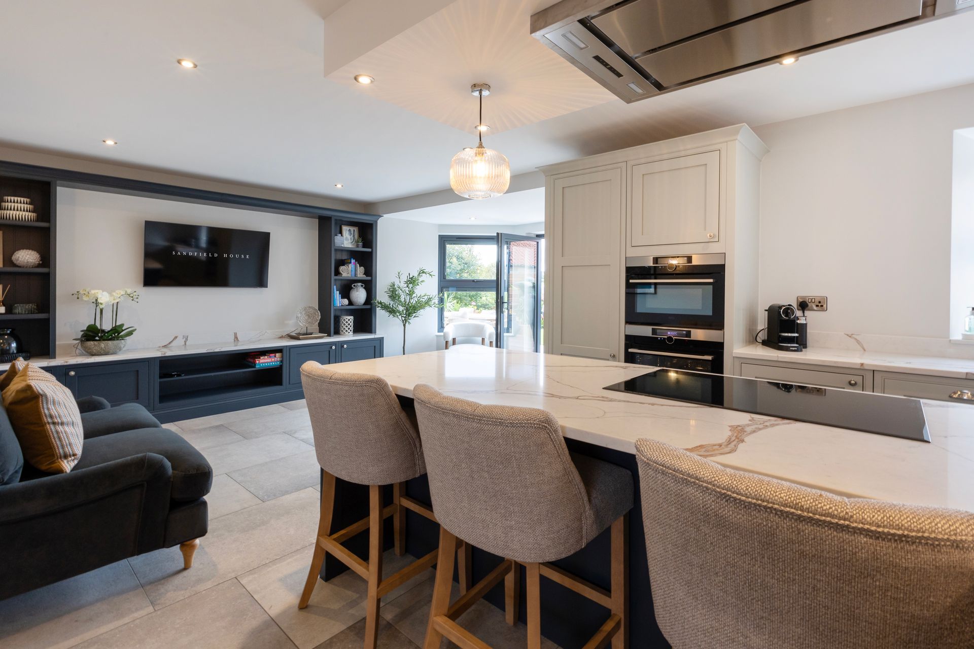 A kitchen with a large island and stools in a living room.