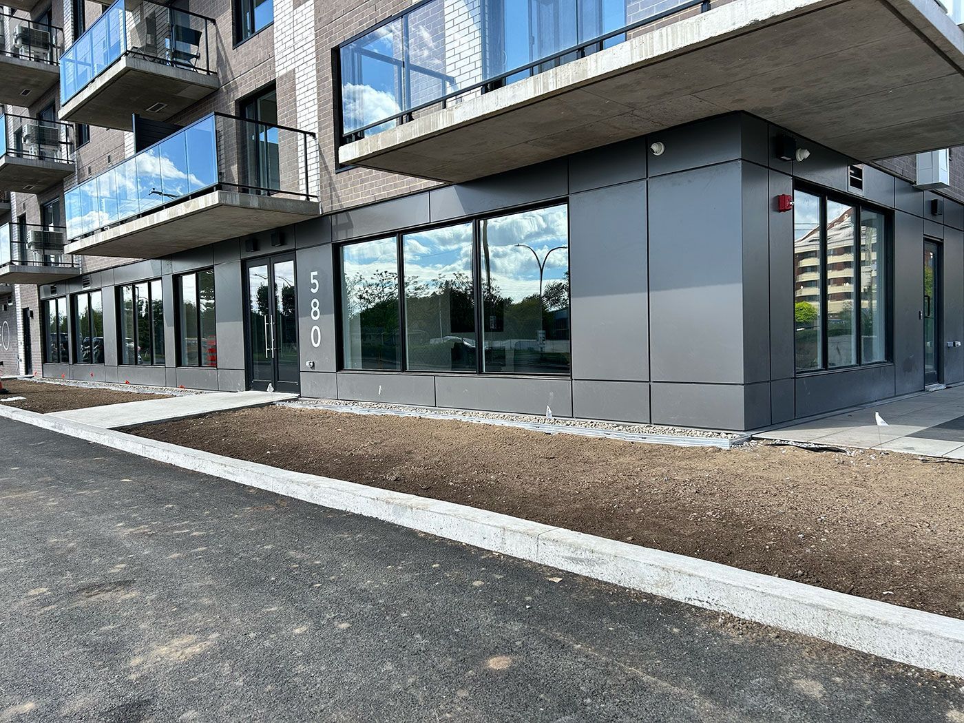 Extérieur d'un bâtiment moderne gris avec de grandes fenêtres et balcons, chemin de gravier devant.
