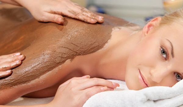 Woman receiving a massage, lying on a table with orchids, candles, and oil bottles.