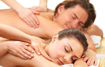 Couple receiving massages at a spa. Woman and man are lying face down, receiving shoulder rubs.
