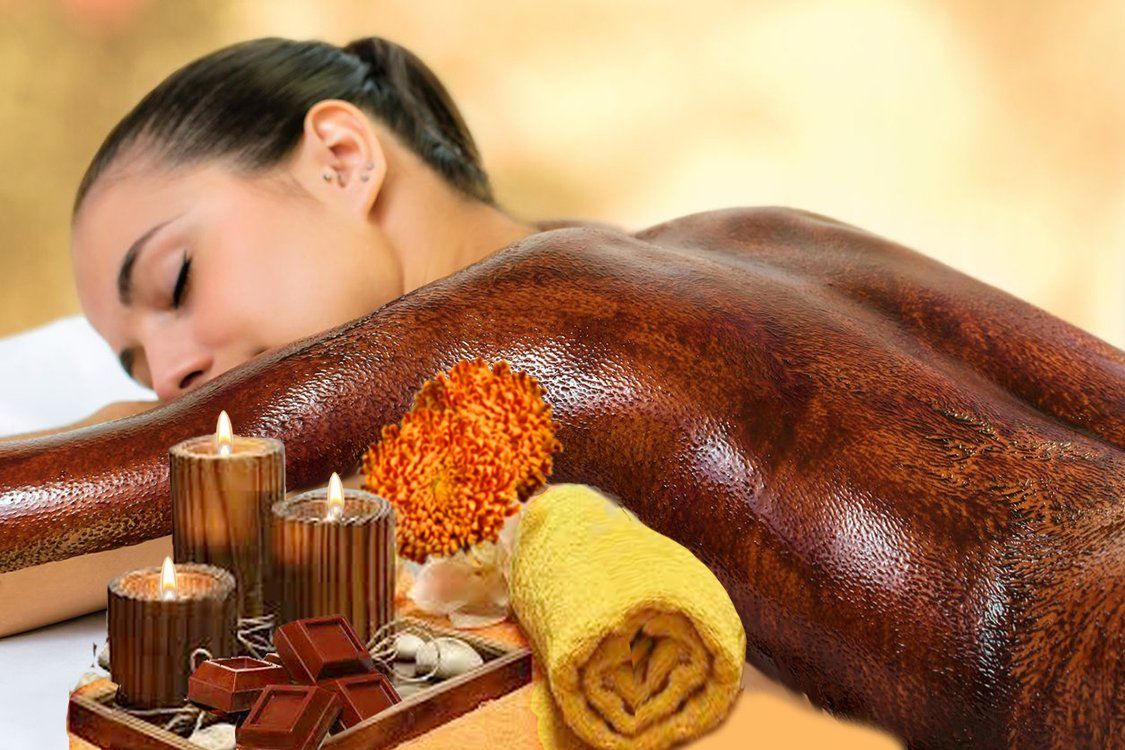 Woman receiving a chocolate spa treatment, candles lit beside her on a wooden tray.