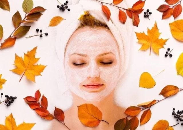 Woman with a face mask surrounded by autumn leaves and berries.