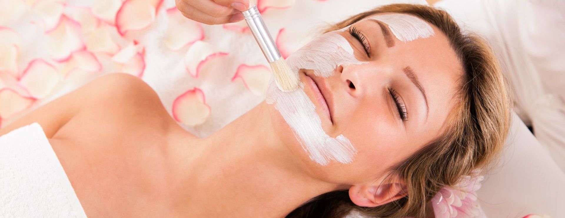 Couple receiving massages on their backs in a spa; lit candles and dried petals present.