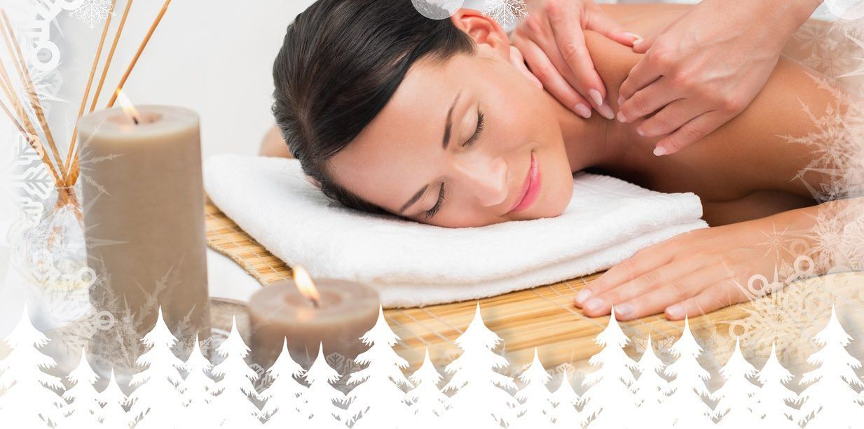 Woman with orange facial mask, smiling while a hand uses a cotton pad to wipe her face in a spa setting.