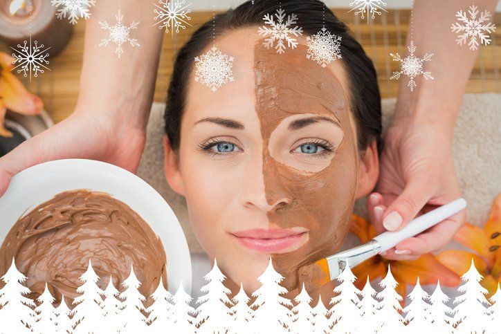 Woman receiving a back scrub at a spa, eyes closed, flower in hair; spa setting with jars of scrub visible.
