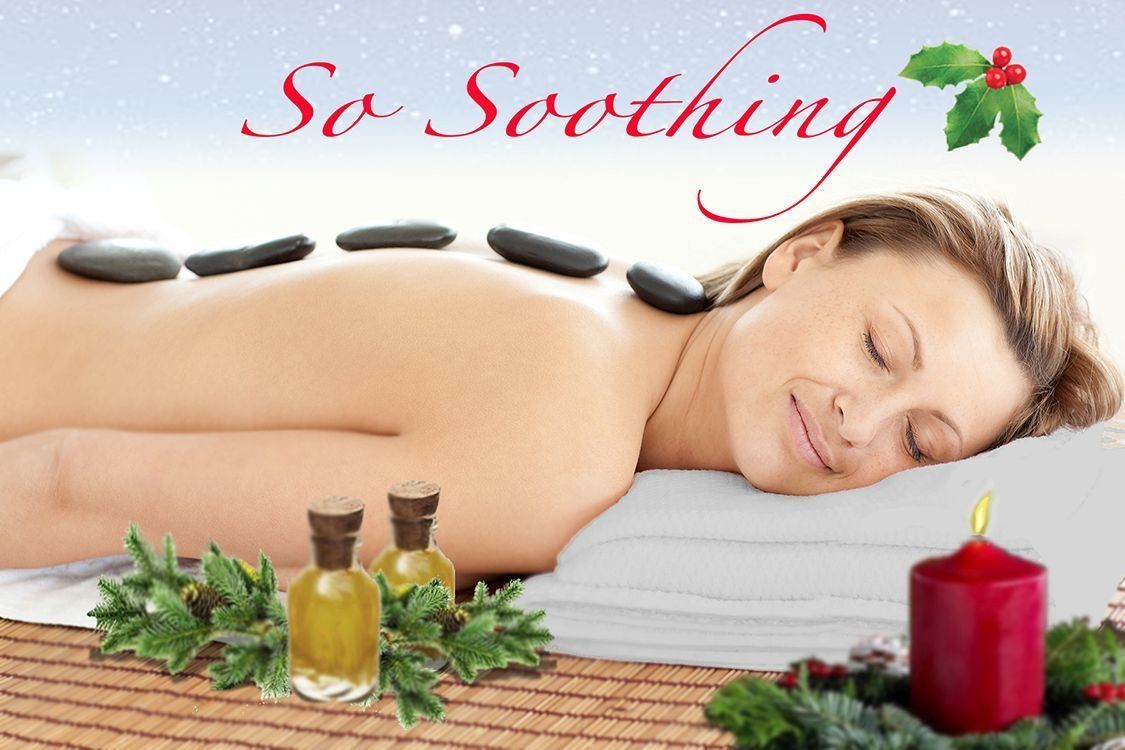 Woman receiving hot stone massage, Christmas setting, relaxed expression.