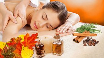 Woman receiving spa treatment, lying relaxed on a white surface, hands resting on chest. Green towels and white flowers are present. Bamboo in the background.