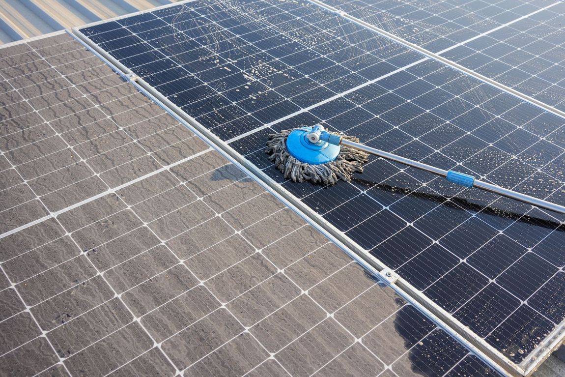 A mop is being used to clean solar panels on a roof.