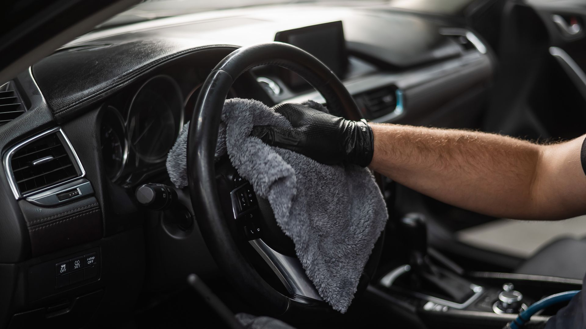 A person is cleaning the steering wheel of a car with a cloth.