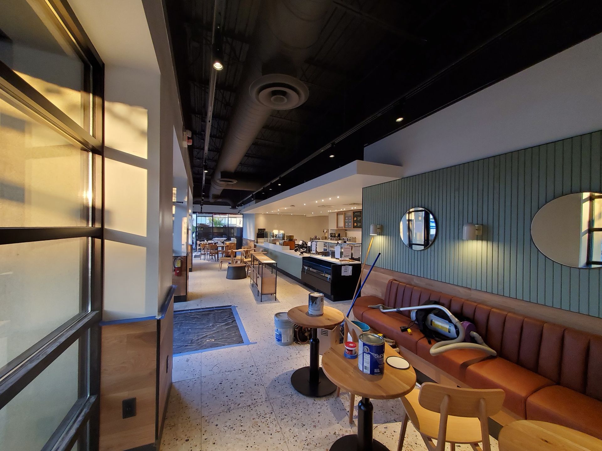 Interior of a cafe with seating, counter, and a view of the outside. The walls are light green and wood.