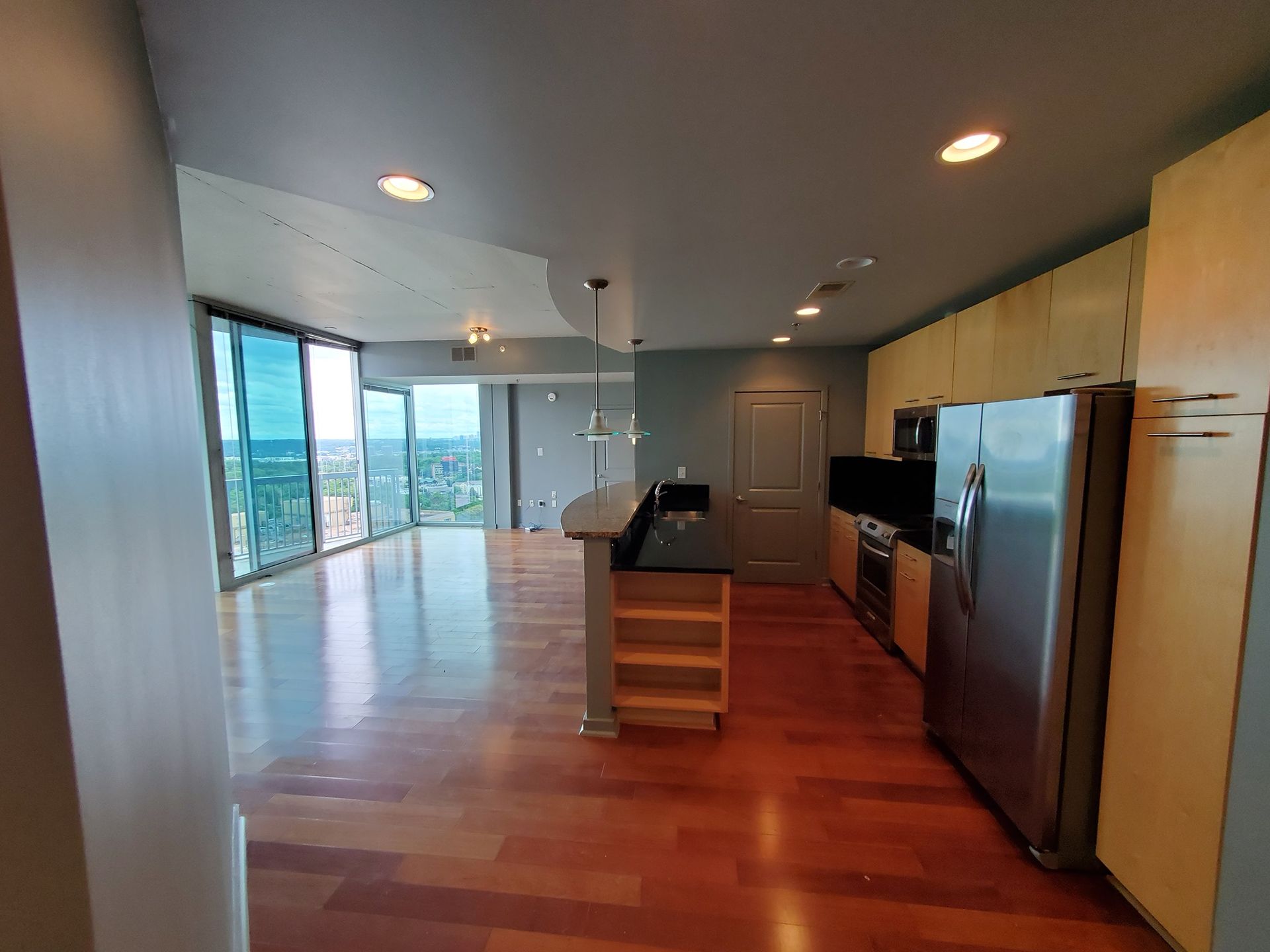 Modern kitchen with wooden floors, stainless steel appliances, and city view through large windows.
