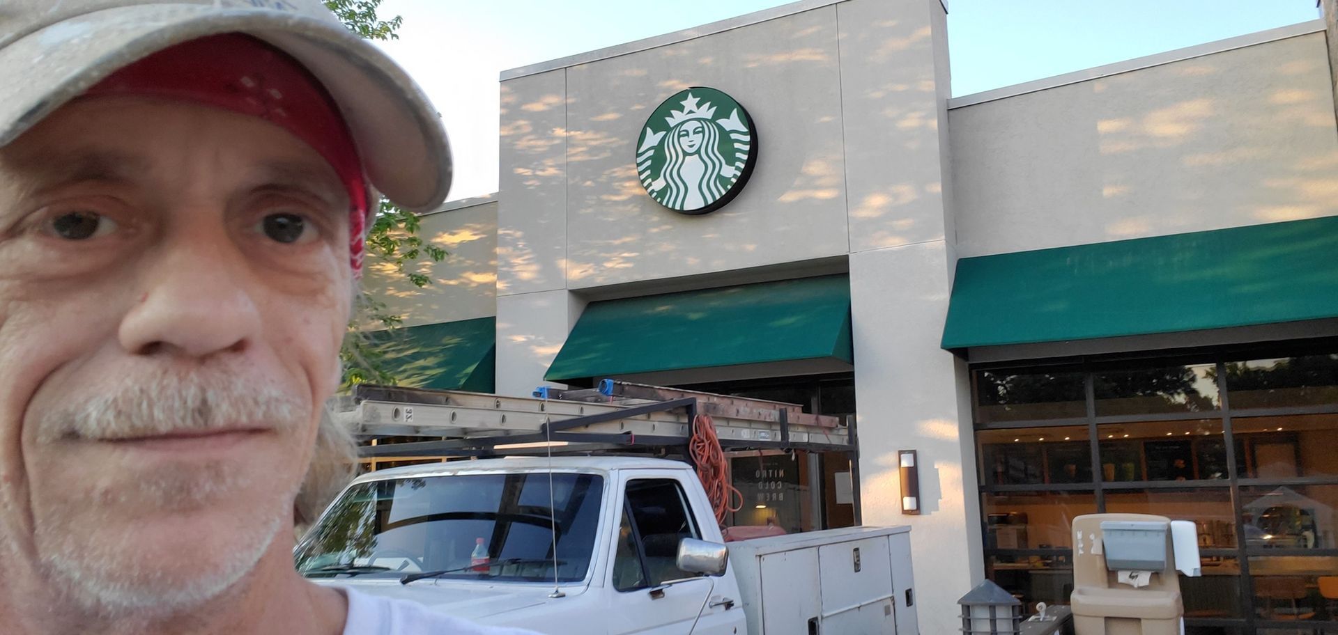 Man in front of a Starbucks with a white truck. He's wearing a cap and bandana.