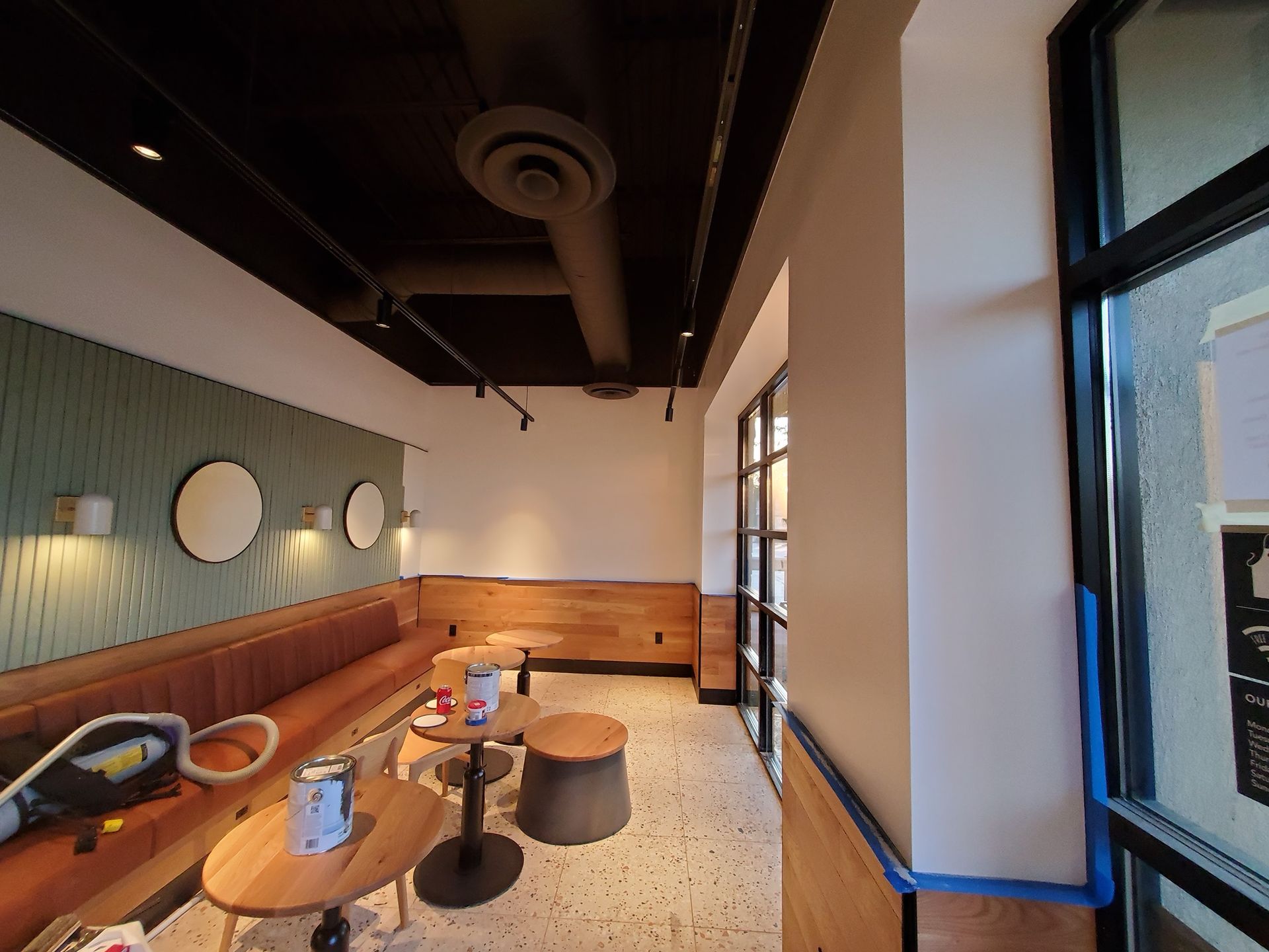 Interior of a cafe with tables, seating, and windows. Walls are painted in white and wood panels.