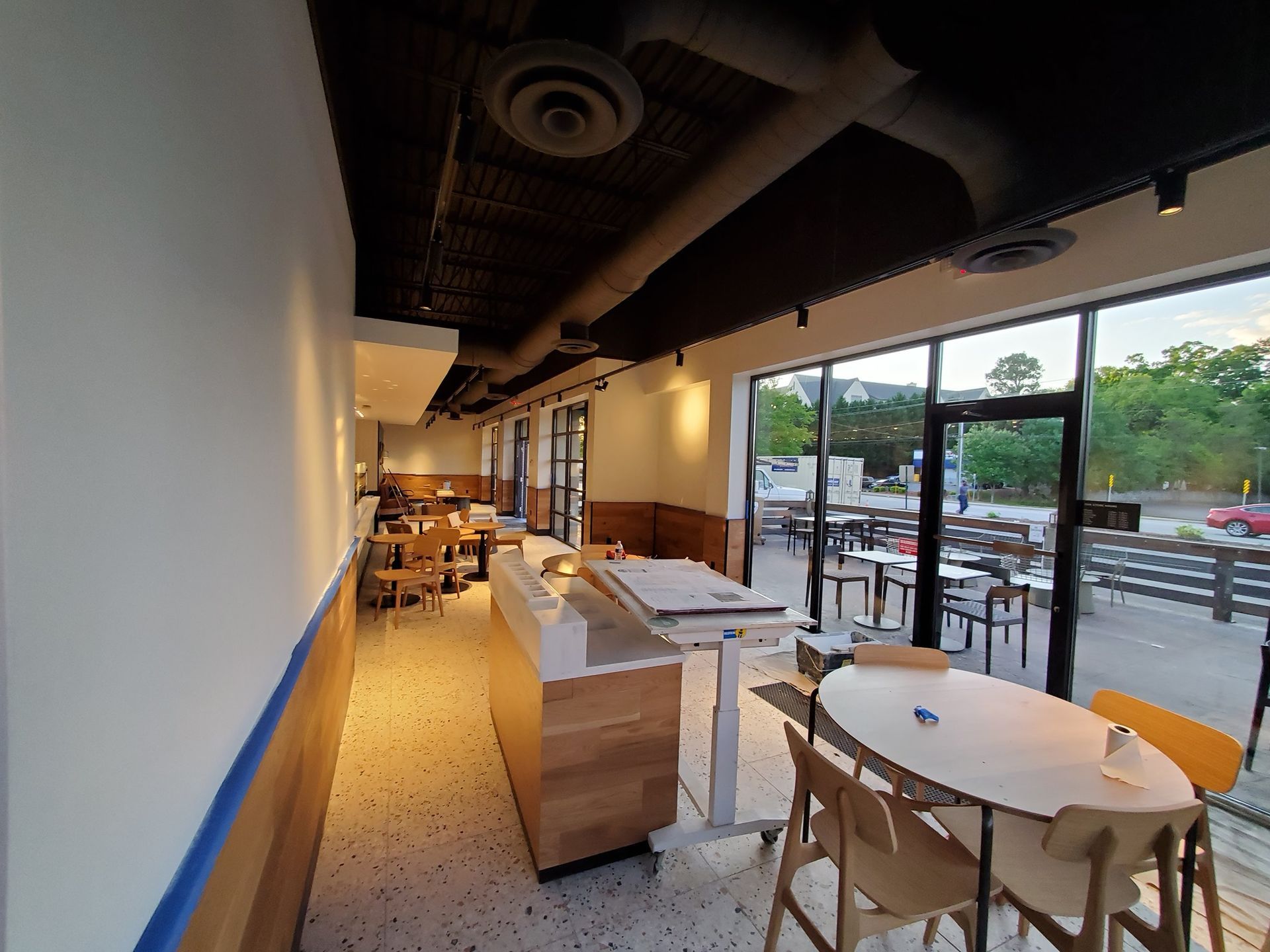 Interior view of a restaurant with tables, chairs, and large windows looking out to an outdoor seating area.