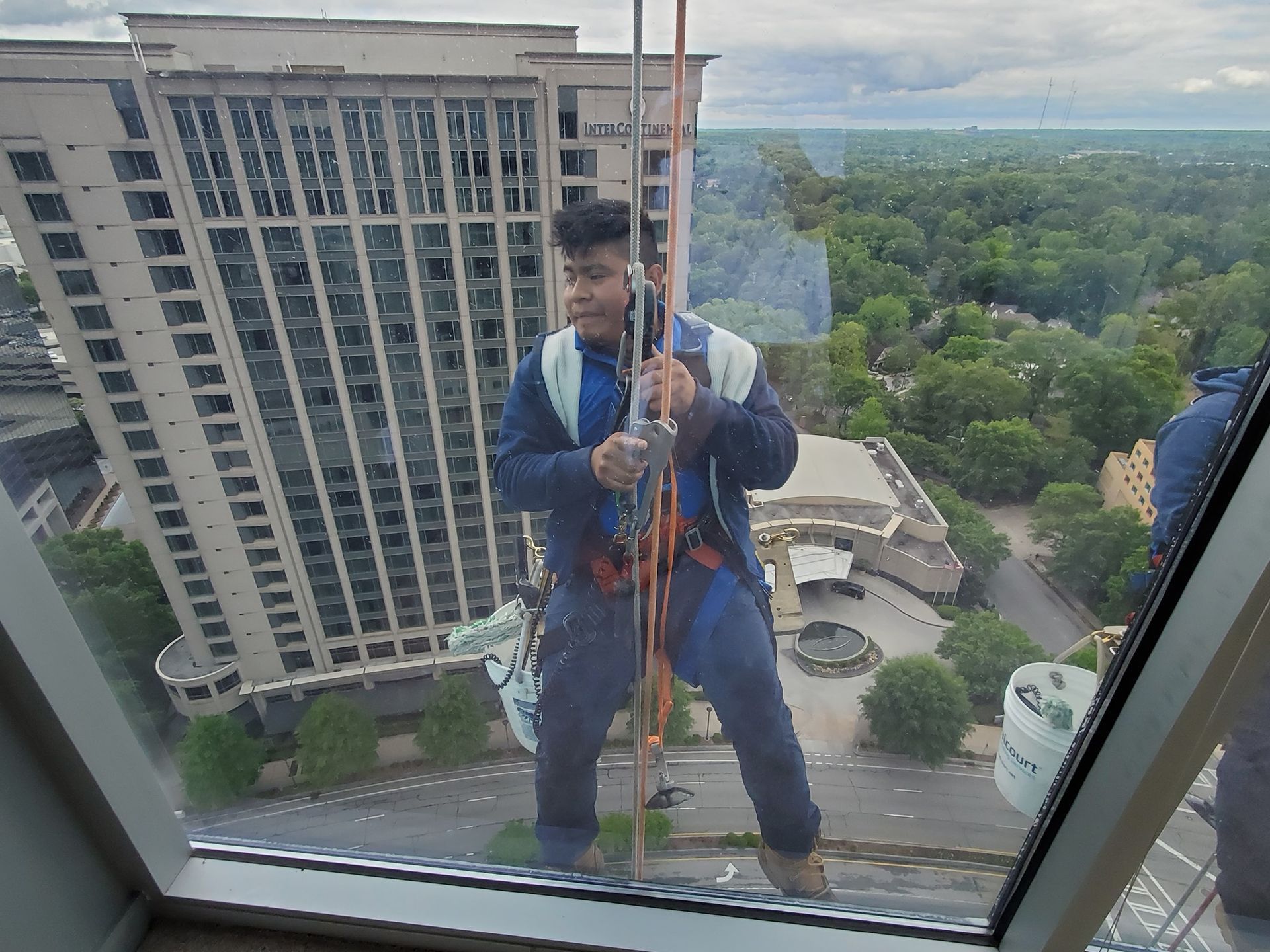 Window washer hanging outside a high-rise building, cleaning windows. Cityscape background.