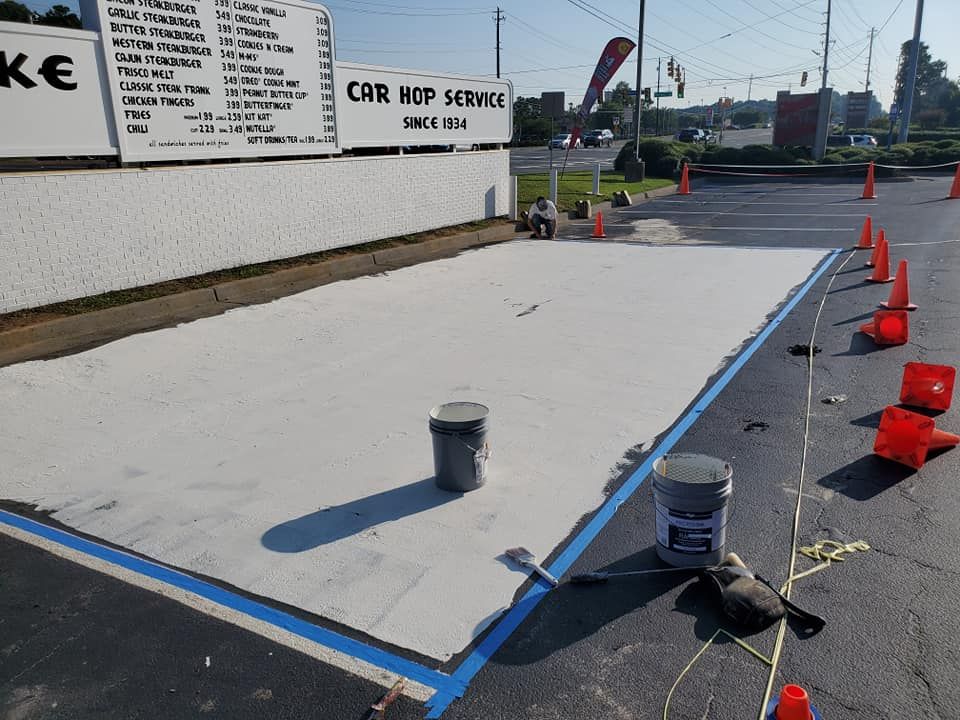 Area of freshly painted concrete, outlined in blue tape, with buckets and traffic cones.