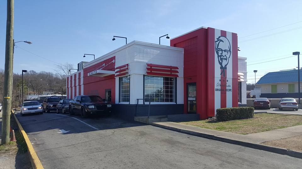 KFC restaurant with red and white facade. Cars in drive-thru lane on sunny day.