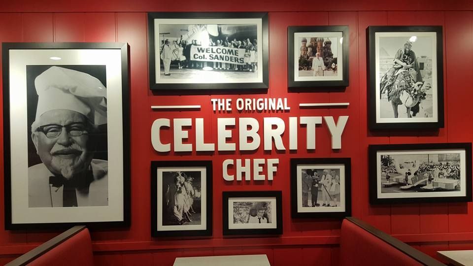 Wall of framed photos and text: “The Original Celebrity Chef” with a portrait of Colonel Sanders.