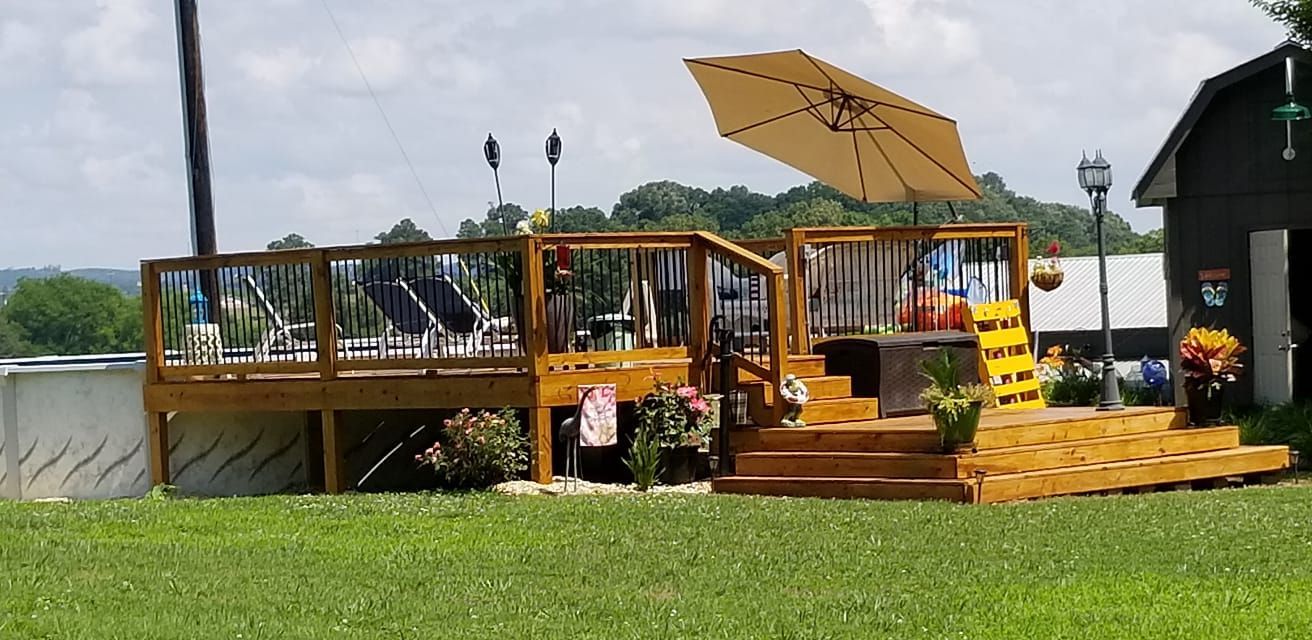 Wooden deck with an umbrella, pool, and a barn.