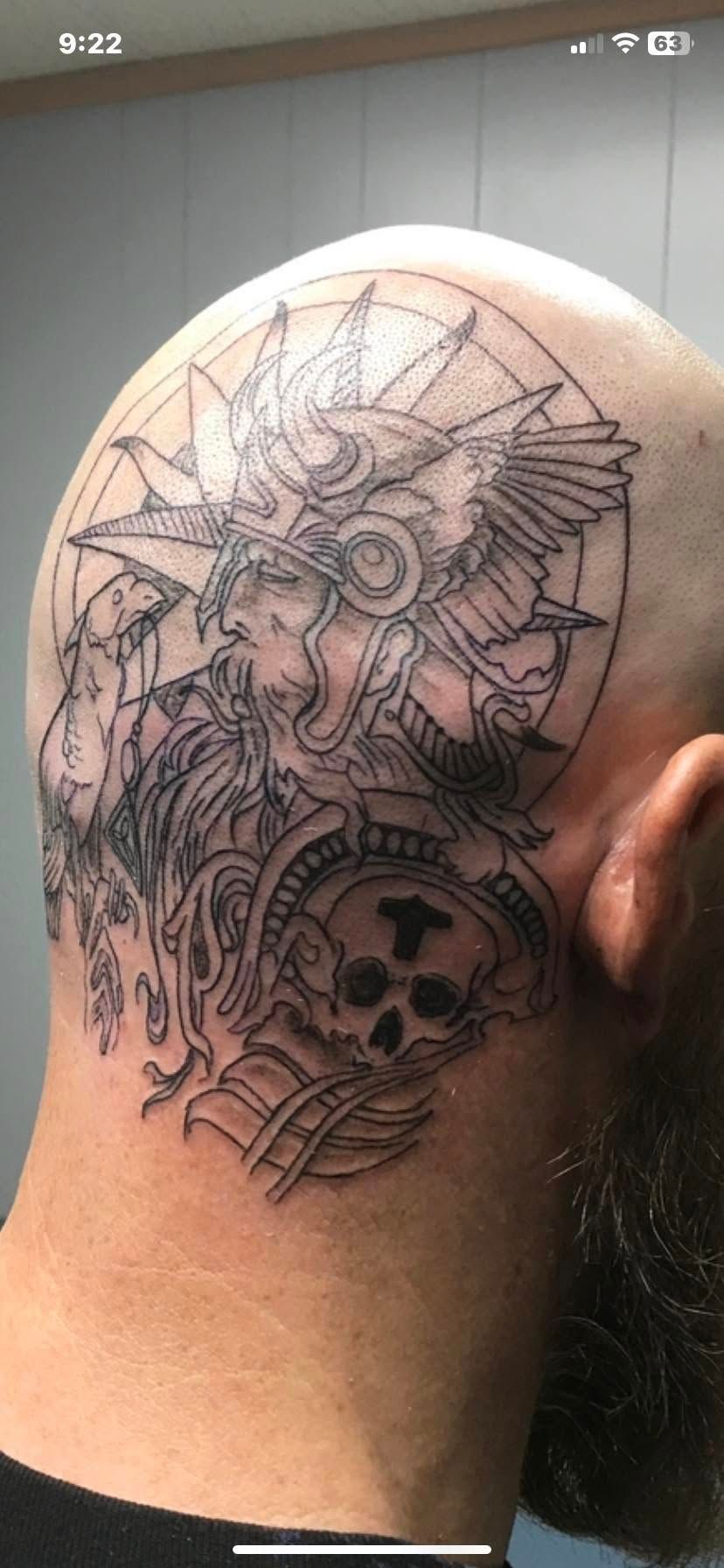 Black and gray tattoo on the back of a shaved head, featuring a skull and warrior figure.