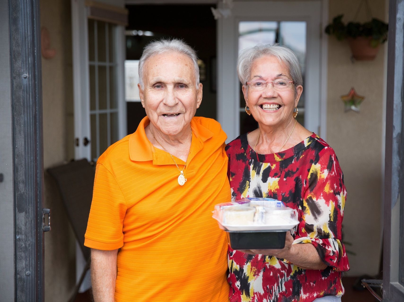 A man and a woman are standing next to each other holding a tray of food.