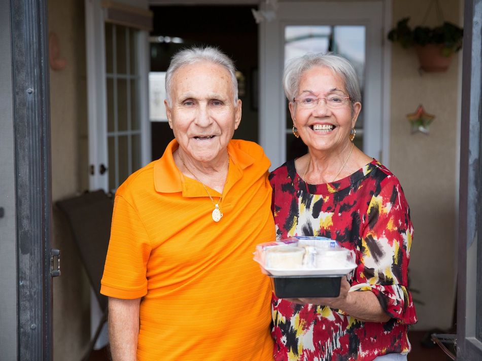 A man and a woman are standing next to each other holding a tray of food.