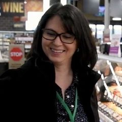 A woman wearing glasses is smiling in front of a sign that says wine