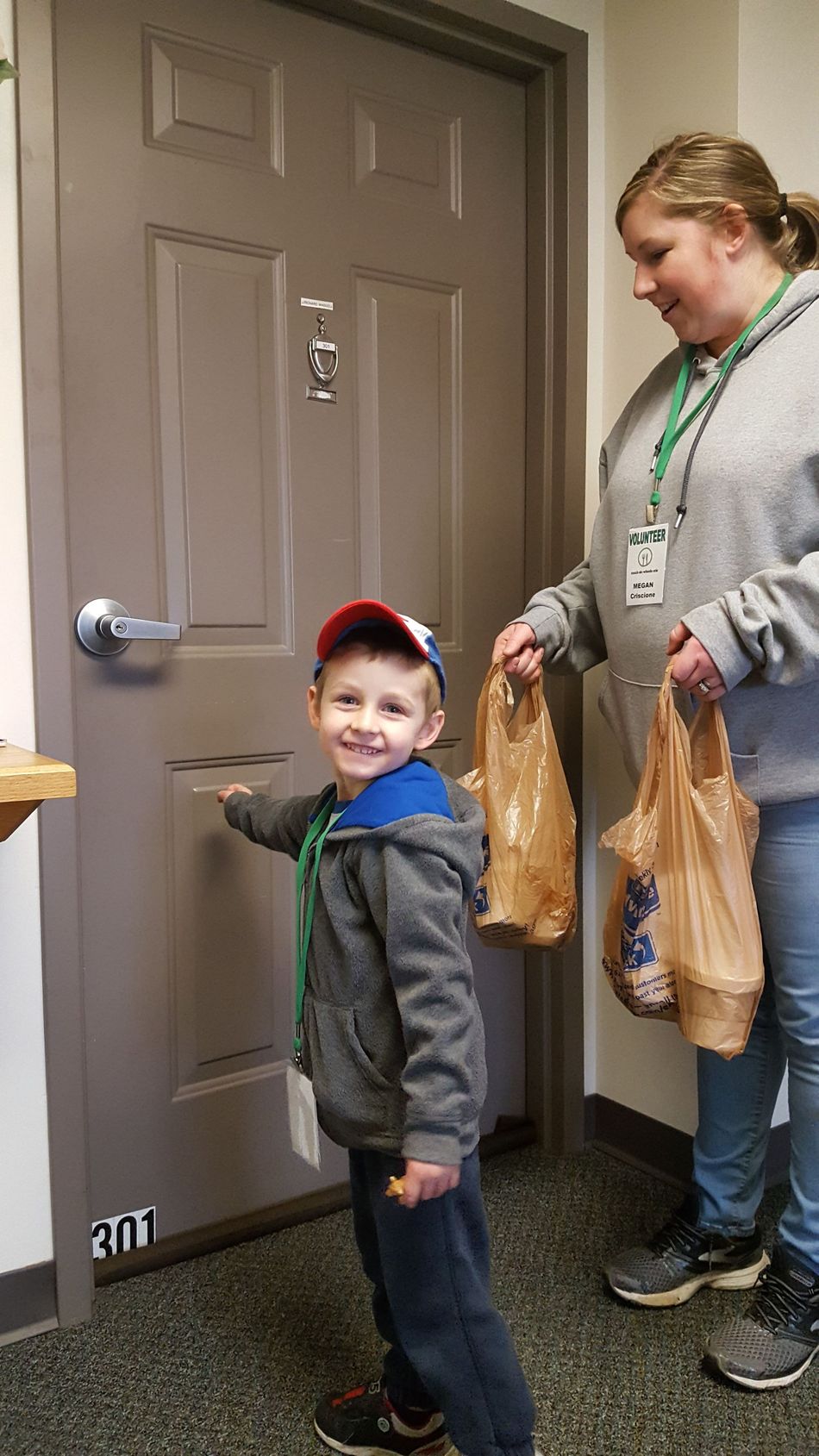 A woman and a boy are standing in front of a door holding bags of food.