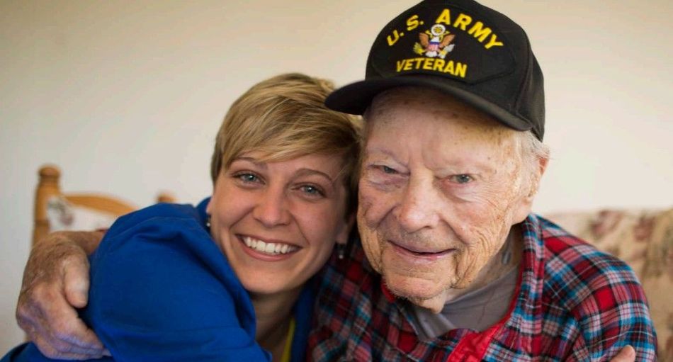 A woman is hugging an older man wearing a us army hat.