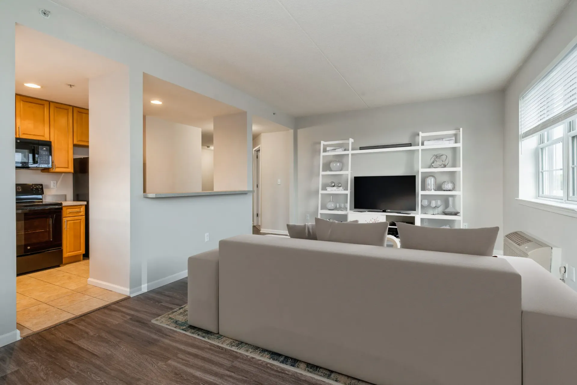 Open-concept living room in a modern apartment with beige sectional, white shelving, and kitchen pass-through Parc at Lyndhurst in Lyndhurst, NJ.