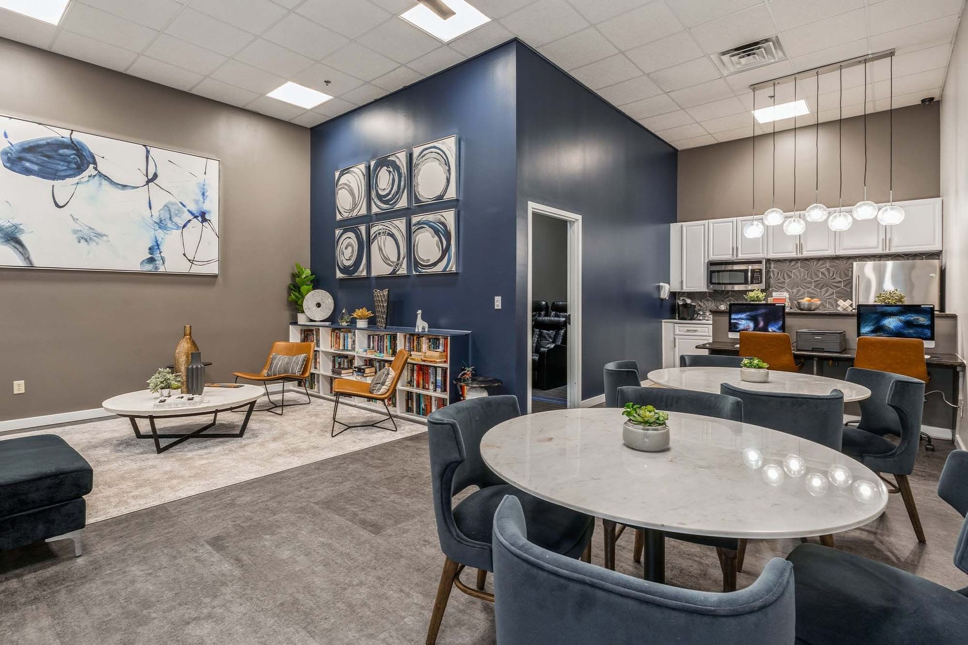 Modern community lounge with round marble tables, blue wall accent, and a kitchenette Parc at Lyndhurst in Lyndhurst, NJ.