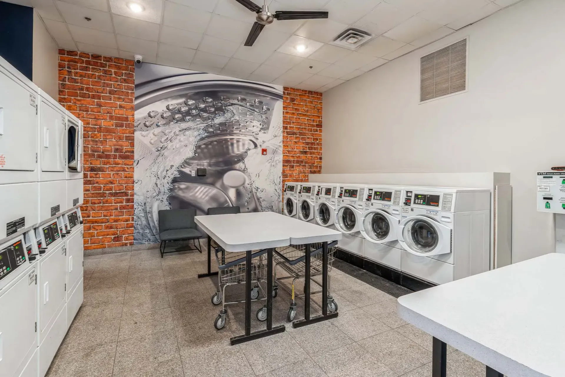 On-site community laundry room with front-loading washers and dryers and folding tables Parc at Lyndhurst in Lyndhurst, NJ.