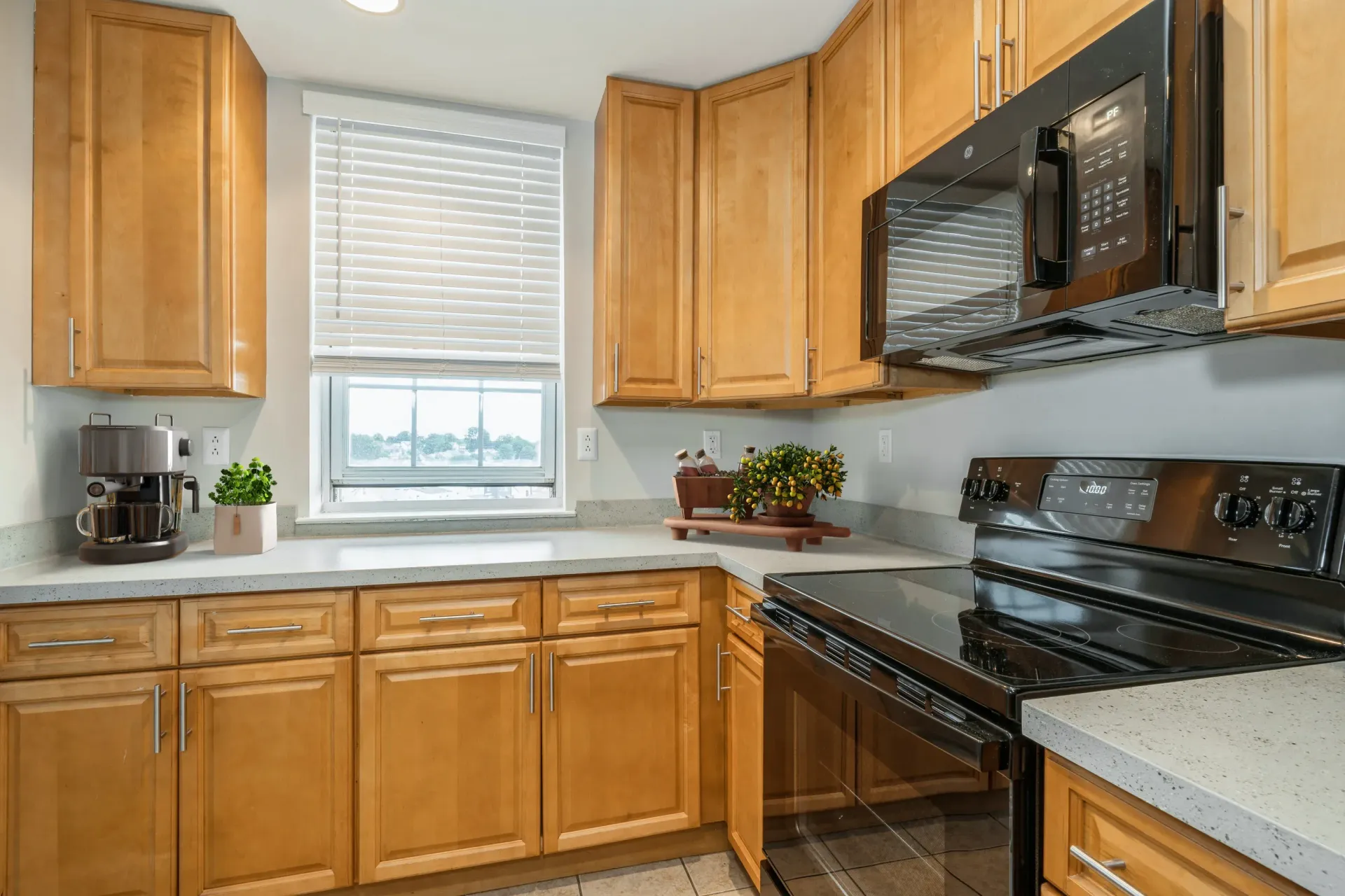 Kitchen with light wood cabinets, black appliances, and a window with blinds Parc at Lyndhurst in Lyndhurst, NJ.