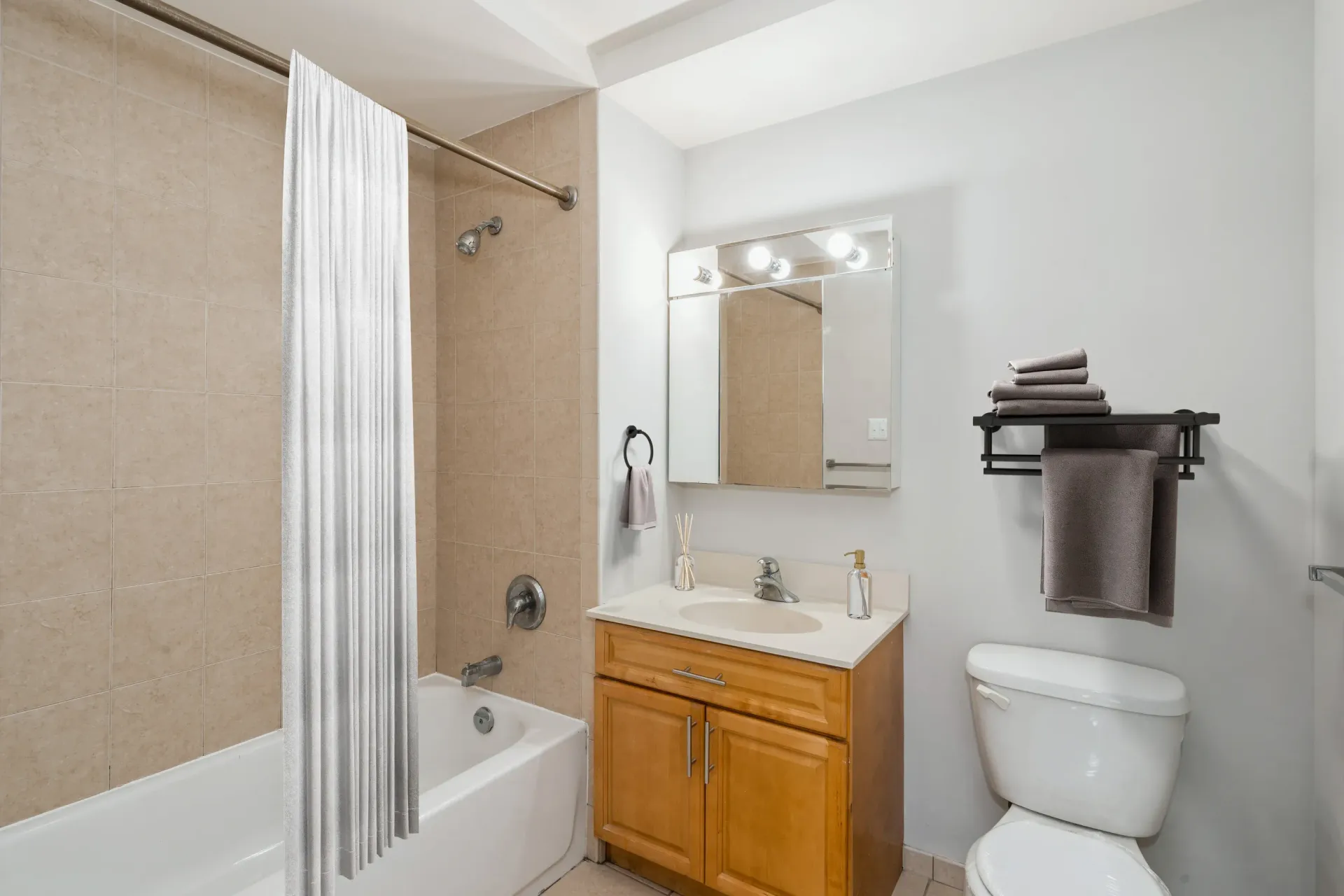 Bathroom with a tub-shower, wood vanity, lit mirror, and towel rack Parc at Lyndhurst in Lyndhurst, NJ.