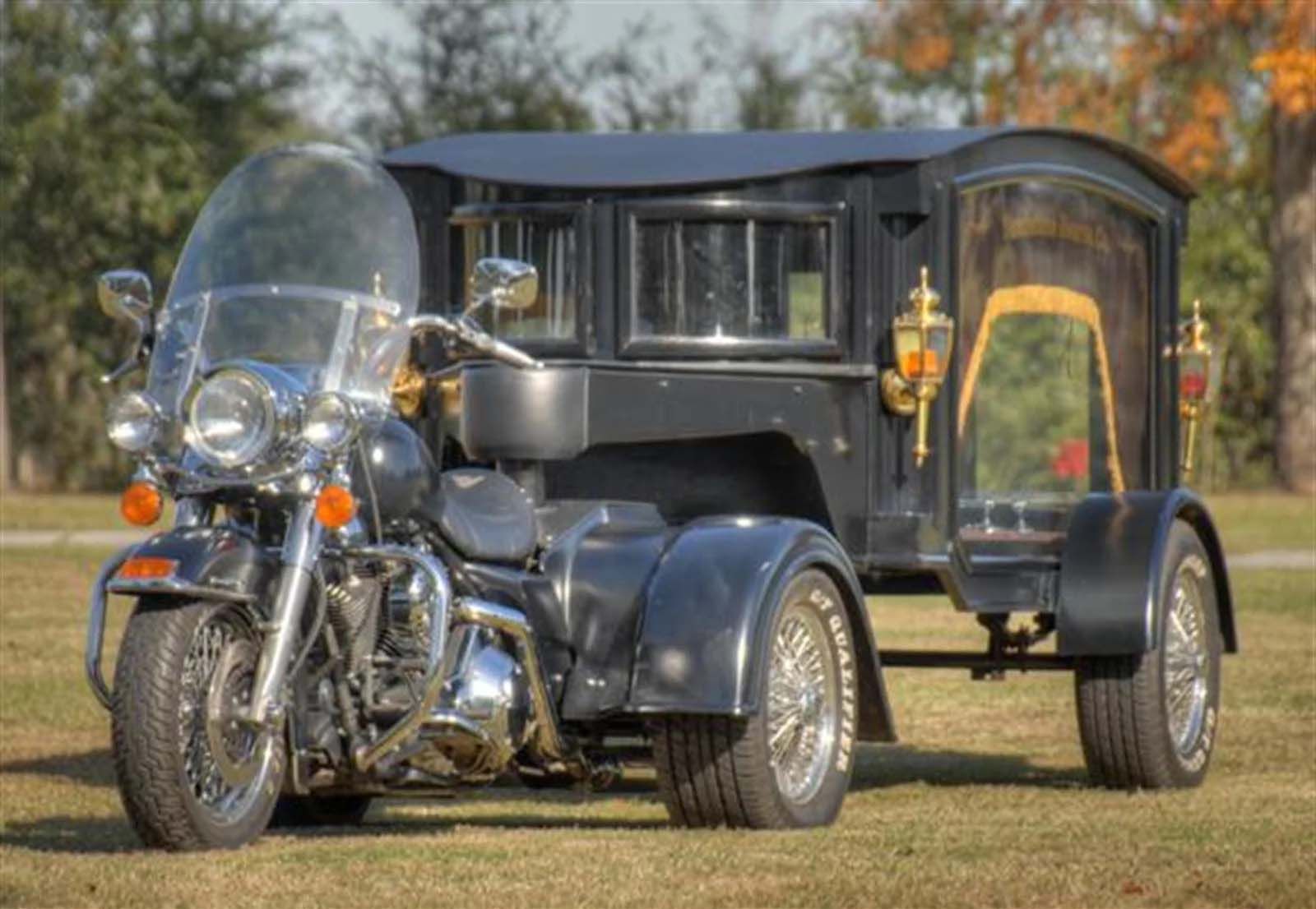 A motorcycle is parked next to a funeral carriage in a field.
