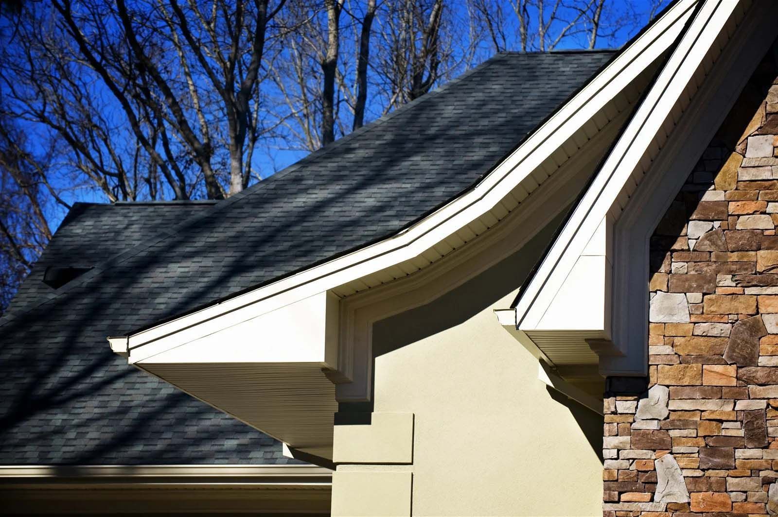 The roof of a house with a stone wall and trees in the background.